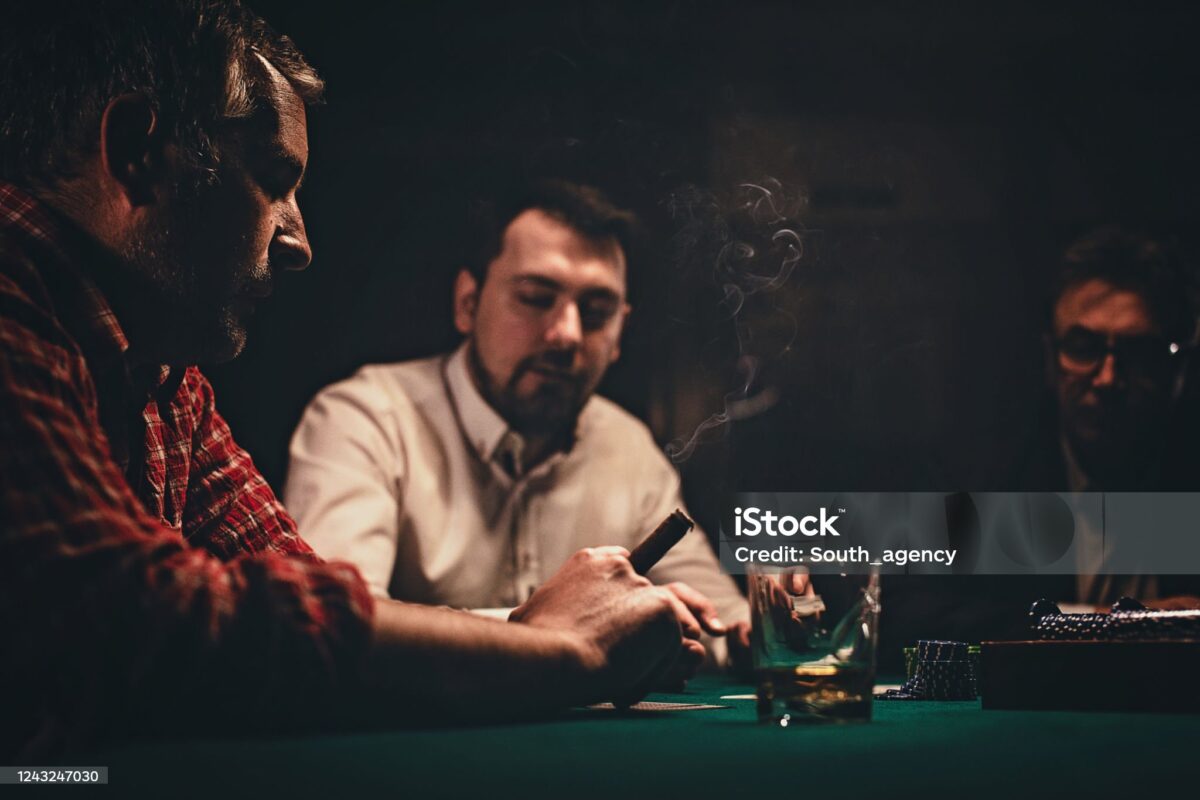 Three people playing cards at a dimly lit table, cigar smoke rising